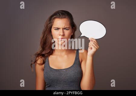 J'ai parfaitement précisé mon point de vue. Photo en studio d'une jeune femme attrayante tenant une bulle de parole vide et regardant en colère contre un fond gris. Banque D'Images