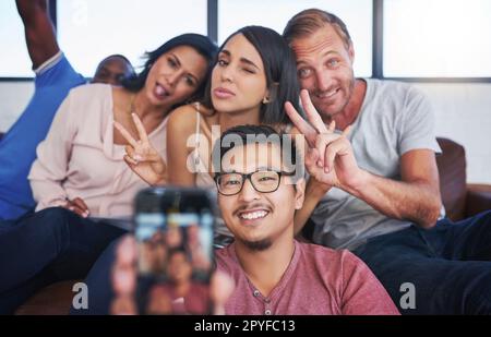 Ils ne se prennent pas trop au sérieux. un groupe heureux de collègues créatifs qui se posent pour un selfie au bureau. Banque D'Images