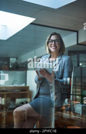 Ça ne me dérange pas les nuits tardives. Portrait rogné d'une femme d'affaires travaillant sur une tablette numérique dans son bureau tard dans la nuit. Banque D'Images