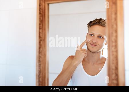 Il prend grand soin de sa peau. un jeune homme appliquant un hydratant sur son visage à la maison. Banque D'Images