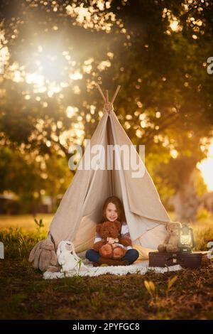 Camping avec Ted. Portrait d'une petite fille mignonne jouant dans son tipi à l'extérieur. Banque D'Images