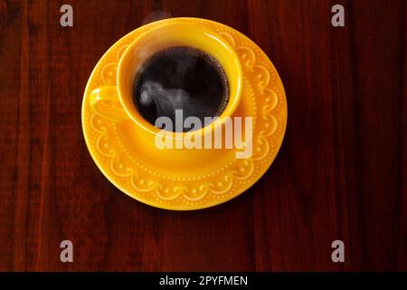 Goiania, Goias, Brésil – 01 mai 2023 : une tasse et une soucoupe jaunes remplies de café chaud à la vapeur sur une table en bois. Banque D'Images