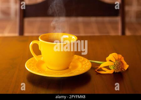 Goiania, Goias, Brésil – 01 mai 2023 : une tasse jaune remplie de café chaud, à la vapeur, avec une soucoupe et un tournesol, sur une table en bois et à l'arrière de Banque D'Images