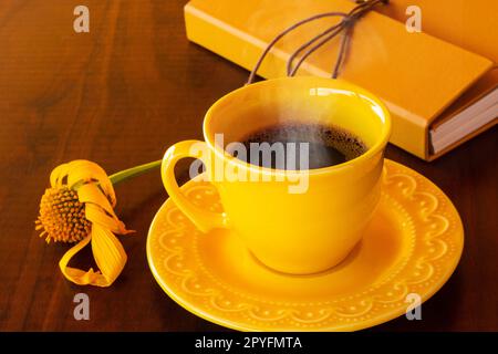 Goias, Brésil – 01 mai 2023 : une tasse jaune remplie de café, avec une soucoupe et un carnet, sur une table en bois, avec un tournesol. Banque D'Images