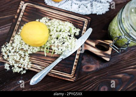 Broyage de citron et de sureau noir sur une planche à découper pour faire une boisson à base de plantes ou un médicament pour la guérison à la maison à partir de sirop de fleurs de sureau. Banque D'Images