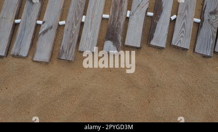 Passerelle en bois sur une plage de sable. Planches de bois irrégulières et humides maintenues ensemble. Le bord de la saison de la plage à l'hôtel. Pas de personnes, copier l'espace. Plage de sable équipée après une tempête ou un cyclone. Tourisme Banque D'Images