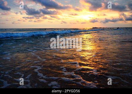 Vague et coucher de soleil sur la mer. Magnifique coucher de soleil. Les vagues mousseuses roulent sur le rivage sablonneux. Vityazevo, Anapa, Mer Noire. Mecque touristique, station thermale. Ciel du soir. Les rayons se réfléchissent sur l'eau Banque D'Images