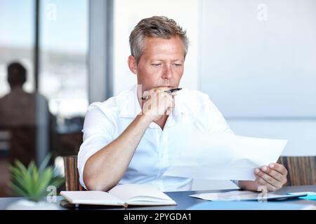 Axé sur le plan en cours. un bel homme d'affaires passant par ses papiers dans le bureau. Banque D'Images