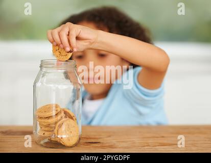 MMM, tellement de cookies juste pour moi. Un jeune garçon mignon saisissant un cookie du pot à biscuits. Banque D'Images