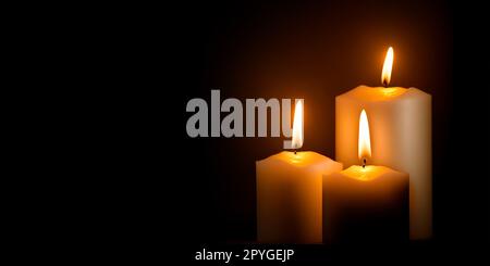Trois bougies de cire blanche qui brûlent dans l'obscurité sur fond sombre Banque D'Images