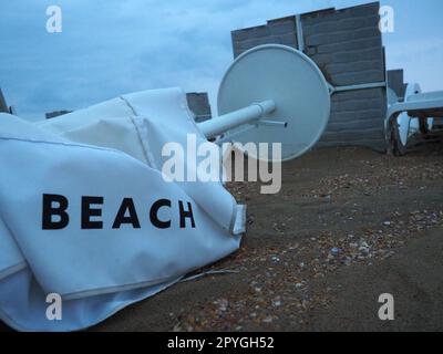 Un parasol était plié sur une plage de sable fin après le mauvais temps. Tempête en mer. Fin de la saison des plages en raison du typhon et du cyclone. Chaises longues, parasols et mobilier d'hôtel. Mot de plage écrit sur blanc Banque D'Images