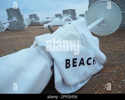 Un parasol était plié sur une plage de sable fin après le mauvais temps. Tempête en mer. Fin de la saison des plages en raison du typhon et du cyclone. Chaises longues, parasols et mobilier d'hôtel. Mot de plage écrit sur blanc Banque D'Images