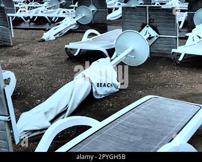 Un parasol était plié sur une plage de sable fin après le mauvais temps. Tempête en mer. Fin de la saison des plages en raison du typhon et du cyclone. Chaises longues, parasols et mobilier d'hôtel. Mot de plage écrit sur blanc. Banque D'Images