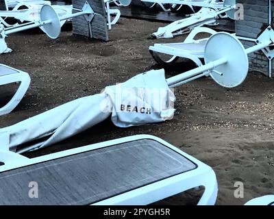 Un parasol était plié sur une plage de sable fin après le mauvais temps. Tempête en mer. Fin de la saison des plages en raison du typhon et du cyclone. Chaises longues, parasols et mobilier d'hôtel. Mot de plage écrit sur blanc Banque D'Images