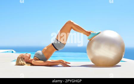 Virage complet du corps. une jeune femme attirante s'entraîner avec une balle d'exercice près d'une piscine. Banque D'Images