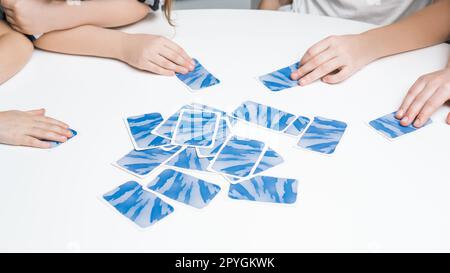 Gros plan recadré méconnaissable mains d'enfants tenant des cartes à jouer bleues sur la table blanche. Jeu de cartes pour le temps. Jeu de moteur Banque D'Images