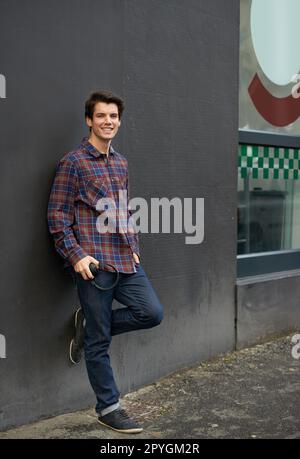 J'adore son style décontracté. Crooped photo d'un jeune homme penché contre un mur à l'extérieur. Banque D'Images