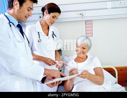 La garder à l'aise et informée. deux médecins fréquentant leur patient senior qui se trouve dans un lit d'hôpital. Banque D'Images