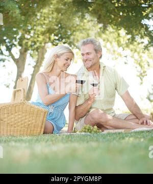 Heres à notre amour. Un mari et une femme heureux de goûter avec un verre de vin pendant qu'ils aiment pique-niquer à l'extérieur dans un parc le jour de l'été. Banque D'Images