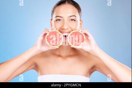 Femme, portrait studio et pamplemousse pour les soins de la peau, cosmétique naturelle ou santé par fond bleu. Modèle, fruit et sourire pour la nutrition, vitamine c ou beauté de soins personnels pour l'esthétique par fond de studio Banque D'Images