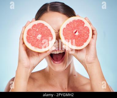 Visage, soins de beauté et femme avec pamplemousse en studio isolé sur un fond bleu. Cosmétiques biologiques, alimentation saine et modèle féminin heureux tenant des fruits pour la vitamine c, les soins du visage et le bien-être. Banque D'Images