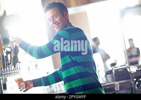 Envie d'une pinte. Un beau jeune barman versant une pinte de bière et vous donnant un grand sourire. Banque D'Images