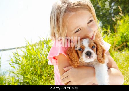 Donner à mon chiot un gros câlin. une jolie petite fille qui embrasse son chiot à l'extérieur. Banque D'Images