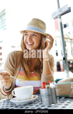 C'est mon café préféré. Une jeune femme remuant son cappucino tout en s'asseyant dans un café-terrasse de la ville. Banque D'Images