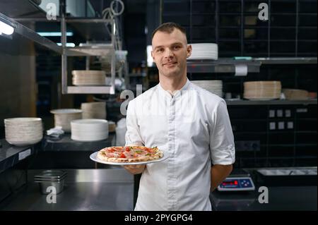 Portrait d'un pizzéiolo masculin présentant une pizza fraîchement cuite Banque D'Images