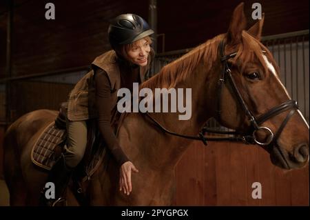 Femme pilote en selle soulève cheval baie affectueusement patting cou Banque D'Images