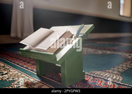 Coran, perles de prière et mosquée avec un livre ouvert et un chapelet dans une salle sainte vide ou un temple prêt à prier. Misbaha islamique, tasbih ou sibha et écriture dans un lieu de culte musulman pour l'eid Banque D'Images