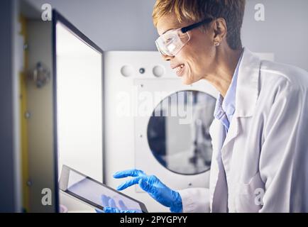 Femme senior, scientifique et tablette en laboratoire pour la recherche, l'innovation scientifique avec des résultats numériques et l'étude scientifique. Incubateur, expérience et biotechnologie avec la technologie, lunettes de sécurité et sourire Banque D'Images