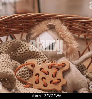 Jouet pour enfants en bois avec des trous pour apprendre le laçage avec cordon orange sur couverture beige dans le panier avec jouet mou lion Banque D'Images