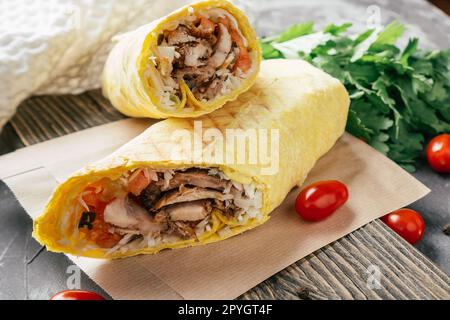 Shawarma classique avec du poulet et des légumes dans du pain pita sur fond foncé en bois avec des tomates cerises et du persil Banque D'Images