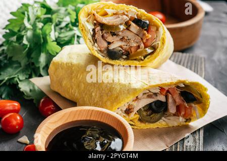 Shawarma mexicain avec sauce piquante, piment jalapeno, olives sur une surface sombre en bois avec tomates cerises et persil vert Banque D'Images