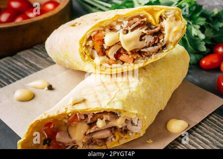 Shawarma au fromage avec sauce au fromage, poulet et légumes en pain pita sur surface en bois, tomates cerises et persil Banque D'Images