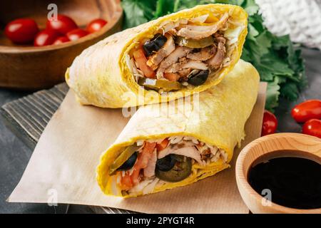 Shawarma mexicain avec sauce piquante, piment jalapeno, olives sur une surface sombre en bois avec tomates cerises et persil vert Banque D'Images