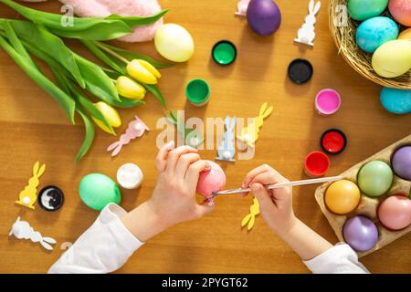 Les mains des enfants peignent un oeuf pour Pâques sur la table en bois à la maison. Préparation pour Pâques. Banque D'Images