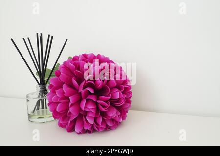 Arrangement avec des bâtonnets d'encens, huile essentielle dans un vase en verre et une fleur artificielle rose-lilas à l'intérieur d'une pièce blanche. Arrière-plan blanc Banque D'Images