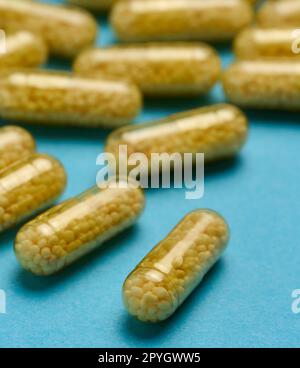 Capsules médicales transparentes avec granules jaunes à l'intérieur sur fond bleu, comprimés pour le traitement, vitamines Banque D'Images