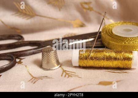 Bobine de fil d'or et ciseaux avec Thimble sur tissu métallique Banque D'Images