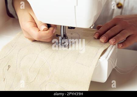 Main couturière utilisant la machine à coudre, mettant le tissu doux blanc avec le contour de point sur la plaque d'aiguille sous le pied-de-biche. Banque D'Images