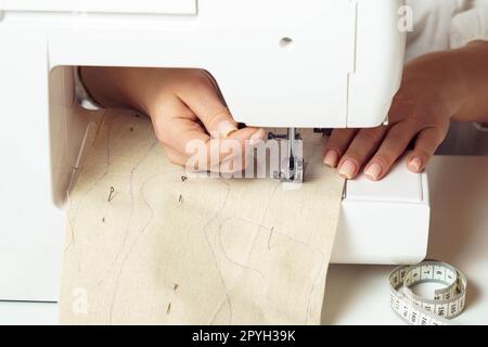 Mains rapprochées recadrées de femme de tailleur à l'aide de la machine à coudre, insérant un motif textile avec des contours de point sous l'aiguille Banque D'Images