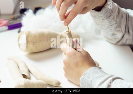 Fermer les mains de couturière féminine méconnaissable coudre des peluches, remplir de coton sur la table dans l'atelier. Magasin pour enfants Banque D'Images