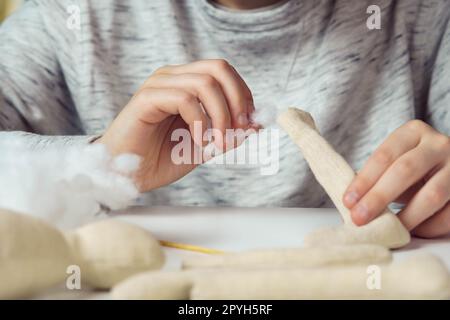 Méconnaissable gros plan femme styliste mains coudre peluche. Créez des pattes et une partie du corps, farcies-les de coton sur la table. Banque D'Images