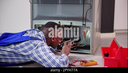 Jeune homme technicien travaillant sur le réfrigérateur avec tournevis Banque D'Images