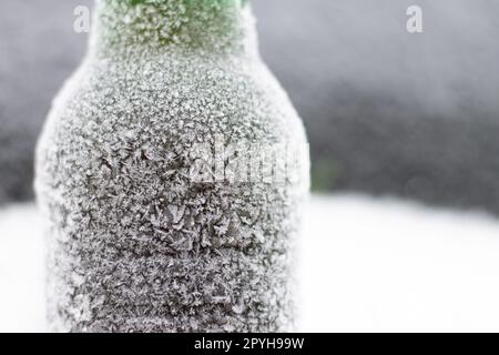 Bouteille de bière partiellement floue recouverte de cerise dans la neige sur fond sombre. Espace de copie Banque D'Images