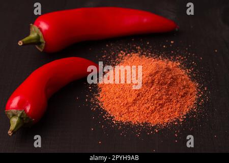 Deux gousses de piments jalapeno rouges chauds et une lame de poudre de poivre sur une surface en bois noir. Banque D'Images