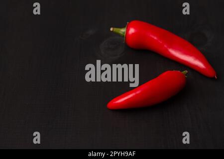 Deux gousses de piments jalapeno rouges chauds sur une surface en bois noir. Espace de copie Banque D'Images