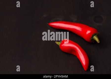 Deux gousses de piments jalapeno rouges chauds sur une surface en bois noir. Espace de copie Banque D'Images